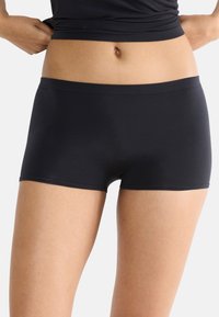 Pantaloni corti in cotone nero elasticizzati con un cinturino liscio, design aderente e cuciture minime. Il tessuto appare morbido e flessibile.