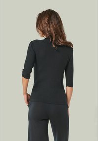 Schwarzer gerippter Pullover mit 3/4-Ärmeln, der einen hohen Halsausschnitt und eine taillierte Silhouette aufweist. Das strukturierte Gewebe verleiht eine dezent ausgefallene Note.