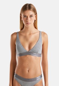 Joven mujer con cabello rubio liso que lleva un sujetador gris y ropa interior a juego, ambos de la marca "United Colors of Benetton".