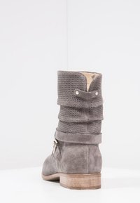 Botín de tobillo gris, holgado, hecho de ante, con parte superior texturizada, tacón plano, hebilla decorativa y detalle de costura a lo largo del cuello.