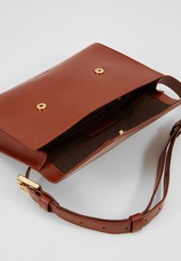 Borsa a mano in pelle marrone con una texture liscia. Presenta dettagli in metallo dorato, una chiusura a scatto esterna e una tracolla regolabile; l'interno è foderato.