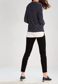 Marinrandig långärmad topp över en vit skjorta, tillsammans med svarta åtsittande byxor och marinblå skor. Slät tyg, avslappnad design.