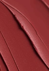Textura roja intensa y profunda con una aplicación suave y gruesa. La superficie presenta surcos sutiles y un acabado brillante, exhibiendo reflejos resplandecientes.