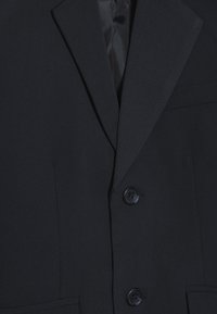 Granatowa marynarka z klapami typu notch, dwoma guzikami i dopasowanym krojem. Wykonana z teksturowanej tkaniny z gładką podszewką.