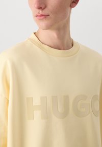Sweatshirt amarelo com um logótipo "HUGO" texturizado. Gola arredondada e corte descontraído, feito de um tecido liso e suave.