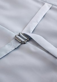 Tissu bleu clair avec une texture lisse, présentant une boucle métallique et un détail de sangle pour un maintien sécurisé.