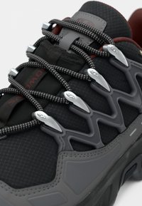 Black athletic shoe with a textured fabric upper, grey accents, tight mesh lacing system, and metallic hardware for secure fit.