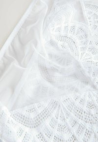 Hvid blonde bralette med detaljerede mønstre, gennemsigtig mesh og tekstureret stof. Kanterne er glat afsluttet med en fin kant.