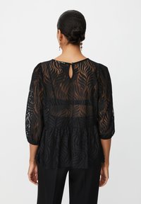 Sort peplum bluse med gennemsigtig blomsterprint, trekvartærmer, nøglehulslukning på ryggen og struktureret stof.