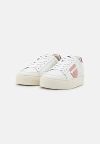 White sneakers with pink accents, leather upper, flat laces, and a thick cream rubber sole. Minimalist design with subtle branding details.