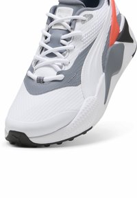 Hvide sneakers med mesh- og lædermaterialer, grå accenter, tekstureret overflade, fremtrædende snøresystem og en kontrasterende sort sål.