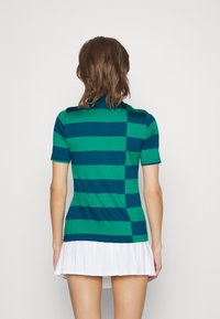 Green and dark blue striped polo shirt with a fitted design, short sleeves, and a ribbed collar, paired with a white pleated skirt.