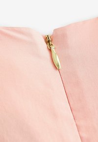 Tissu rose à la texture lisse avec une fermeture éclair en métal doré en haut, mettant en avant des lignes épurées et un design simple.