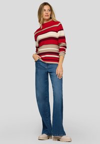 Rot-beiger gestreifter Pullover mit rundem Ausschnitt, kombiniert mit blauen ausgestellten Jeans und klobigen beigen Schuhen.