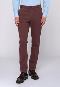 Burgundské kalhoty z texturované tkaniny, s úzkým střihem, bočními kapsami a zapínáním na knoflík. V kombinaci s černými mokasíny.