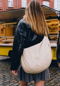 Borsa slouchy beige realizzata in materiale morbido, con una texture trapuntata e un discreto marchio sul davanti. Indossata a spalla, abbinata a un giubbotto nero.