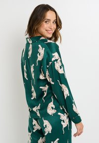 Blusa verde in satin con stampa tigre ripetuta, maniche lunghe e colletto classico. Mostra la vista posteriore con spalle scese.