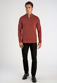 Pitkähihainen, vetoketjullinen villapaita tummanpunaisena, neulottu rakenne, yhdistetty mustiin housuihin ja kiiltäviin mustiin loafer-kengiin. Yksinkertainen, urheilullinen muotoilu.