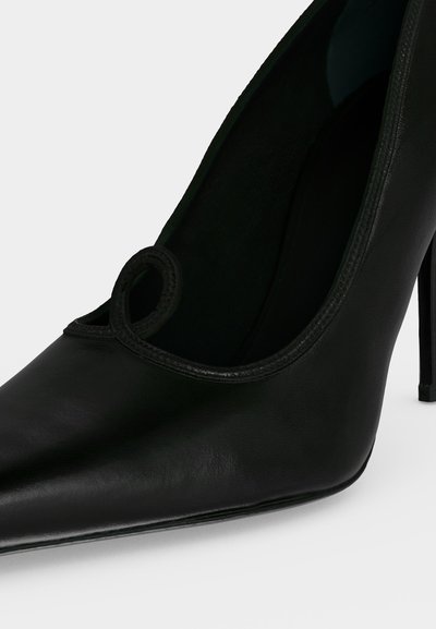 Chaussure à talon haut en cuir noir à bout pointu avec un talon aiguilles fin et un détail en boucle près de l'ouverture.