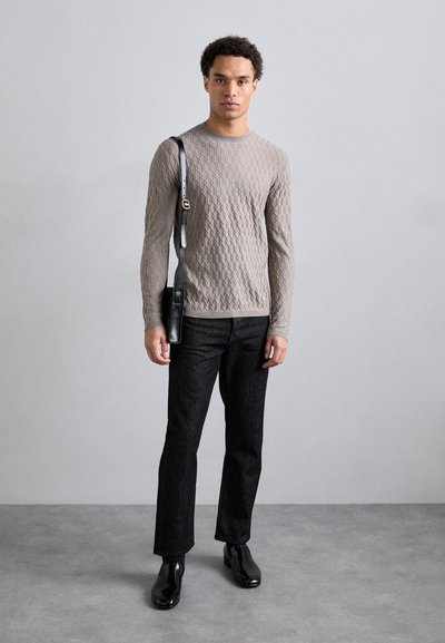 Bežs teksturēts džemperis, melni džinsi un spīdīgas melnas zābaki. Melnā plecu soma ar siksnu atpūšas uz pleca.