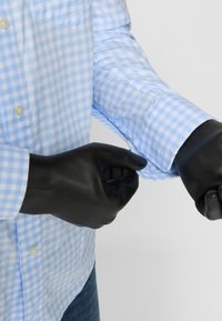 Sorte gummihandsker båret på hænderne, parret med en lys blå ginghamrute skjorte med knapper og optrukkede ærmer.