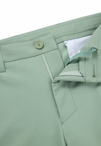 Jasnozielone spodnie wykonane z gładkiego materiału, z zapięciem na guzik, zamkiem błyskawicznym i detalami kieszeniami po bokach; posiadają tonalne szwy i metkę marki.