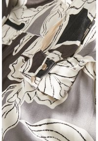 Siden skjorta med ett svävande mönster som har svarta och vita blommönster på en grå bakgrund. Tryckknappar som detalj på kragen.