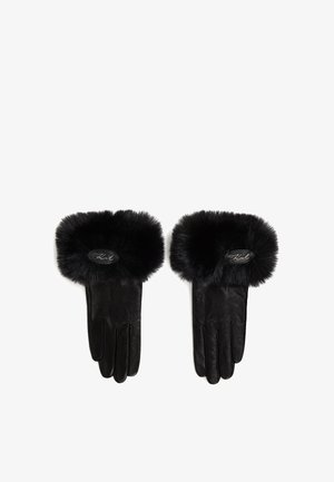 Gants en cuir noir avec un poignet en fausse fourrure noire pelucheuse. Présente un patch logo ovale au poignet. Texture lisse avec une forme structurée.