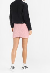 Black denim jacket with a cropped design, paired with a light pink corduroy mini skirt featuring a frayed hem, worn with white sneakers.