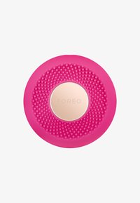 Rosa silikon ansiktsrengöringsapparat med texturerad yta, cirkulär form och en central guldtonad accent med varumärket "FOREO."