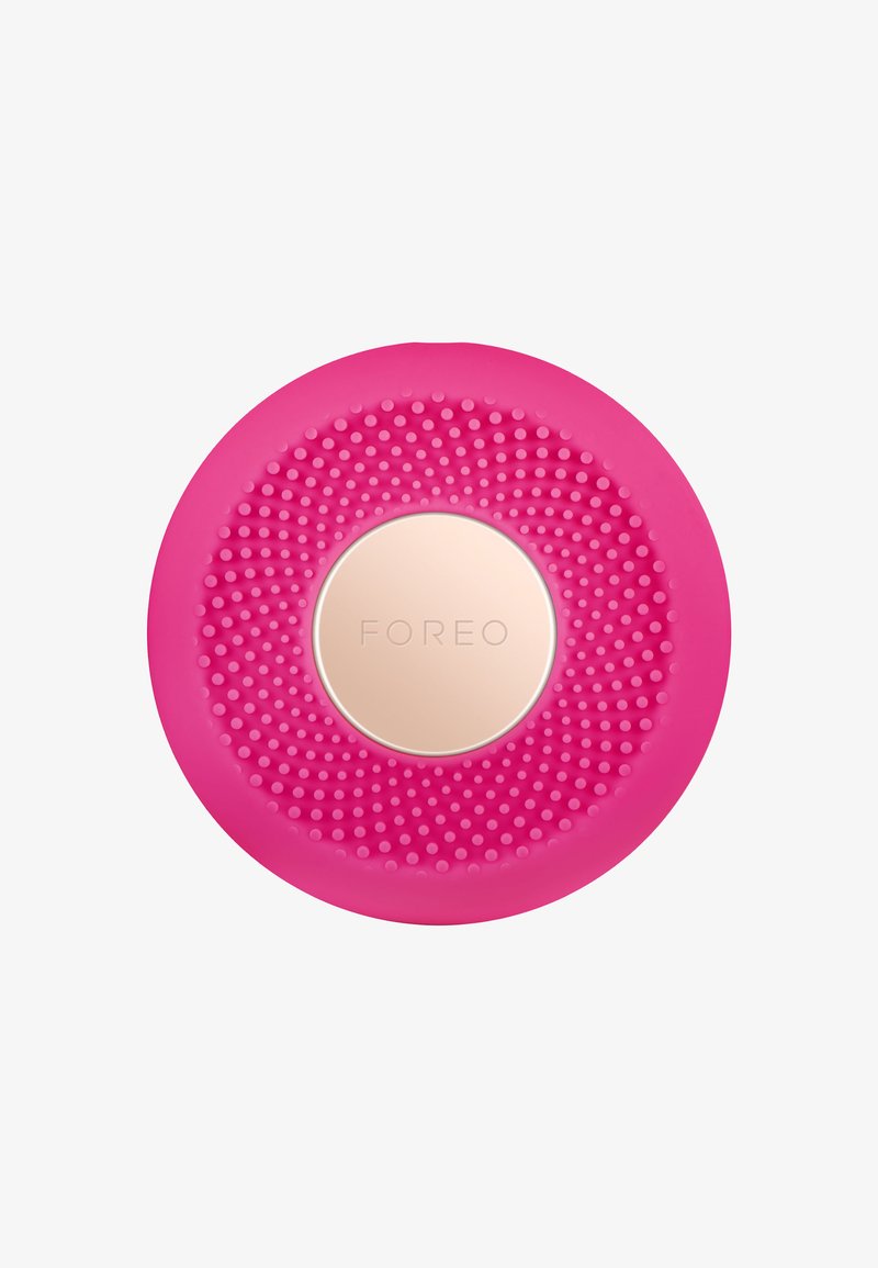 Rosa silikon ansiktsrengöringsapparat med texturerad yta, cirkulär form och en central guldtonad accent med varumärket "FOREO."