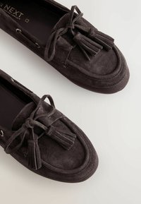 Mocassins en daim marron foncé avec détails pompons et laçage à l'avant, présentés en plongée sur un fond clair.