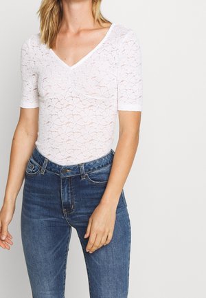 Witte kanten bodysuit met korte mouwen en een V-hals, met een bloemenpatroon. Gecombineerd met donker denim high-waisted jeans.