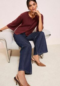 Burgundský pletený kardigan s trojštvrťovými rukávmi a gombíkovým zapínaním; skombinovaný s tmavými širšími džínsami a hnedými lodičkami s úzkou špičkou.