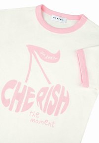 T-shirt blanche à côtes avec bordures roses et impression graphique de cerises et du texte "CHÉRISSEZ le moment" de "OH APRIL" sur le devant.