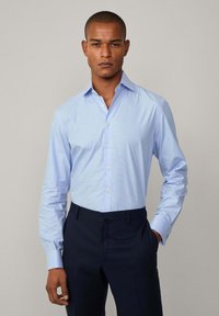 Camicia azzurra chiaro con motivo a quadretti, maniche lunghe e colletto classico, abbinata a pantaloni blu scuri.