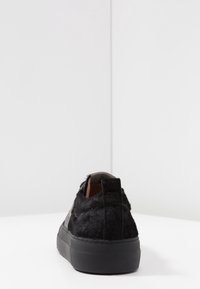 Svart fuskpäls sneakers med strukturerad yta, rund form, tjock gummisula och dragflik på baksidan för enkel påtagning.