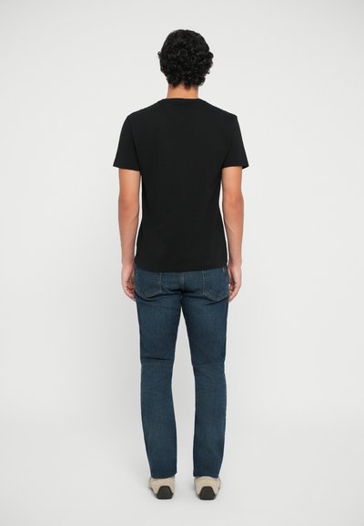 Μαύρο κοντομάνικο μπλουζάκι από πίσω, συνδυασμένο με μπλε τζιν. Το ύφασμα του μπλουζακιού φαίνεται λείο και τα τζιν έχουν κλασική γραμμή με τσέπες.