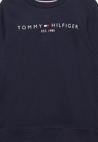 Marineblaues Sweatshirt mit Rundhalsausschnitt, gerippten Bündchen und Saum. Auf der Vorderseite sind "TOMMY HILFIGER" und "EST. 1985" in weißer Stickerei zu sehen.