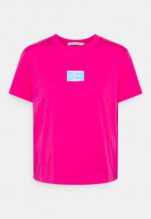 T-shirt in cotone fucsia con scollo rotondo, maniche corte e una toppa rettangolare blu con logo sulla parte anteriore. Tessuto liscio e vestibilità comoda.