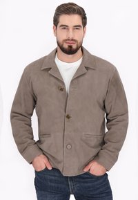 Jachetă din suede maro cu guler decupat, două închideri cu nasturi și buzunare frontale. Textură netedă, design ajustat și detalii de cusătură vizibile.