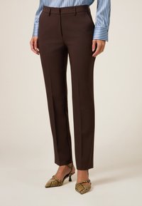 Pantalones marrones a medida con una silueta elegante, que presentan una textura suave y trabillas para cinturón, combinados con tacones de estampado de serpiente.