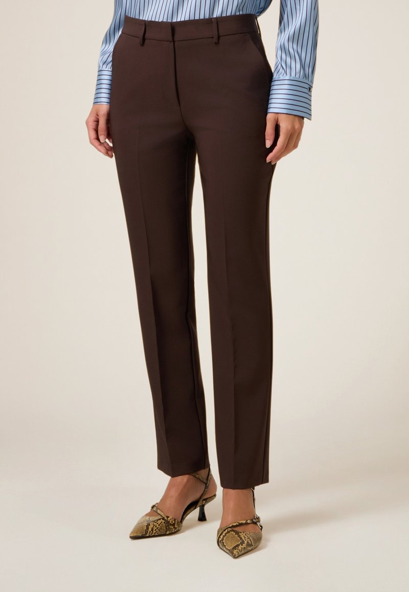 Pantalones marrones a medida con una silueta elegante, que presentan una textura suave y trabillas para cinturón, combinados con tacones de estampado de serpiente.
