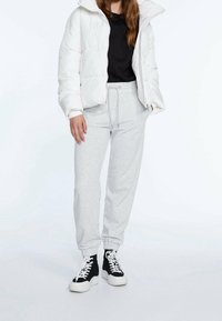 Chaqueta de plumas blanca, camiseta negra, pantalones de chándal gris claro, zapatillas altas negras con suelas blancas, con diseño de cordones y puños elásticos.