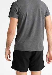 Harmaa lyhythihainen paita pyöreällä kaula-aukolla ja mustilla sivuvarsilla, yhdistettynä mustiin urheilushortsisiin. Ei näkyviä kuvia tai korostuksia.