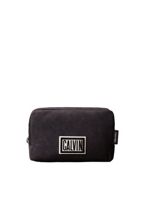 Pochette rectangulaire noire avec une fermeture éclair et un patch blanc sur lequel est inscrit "CALVIN" sur le devant, avec une petite étiquette Calvin Klein sur le côté.