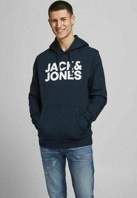 Sudadera azul marino con logo blanco "JACK & JONES", con un bolsillo tipo canguro y capucha con cordón. Combinada con jeans desgastados de un tono azul claro.