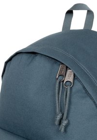Texturerad, mörkblå ryggsäck med rundad topp, som har ett blixtlåsstängning med dubbla metallblixtlås och dragsnoddar på framsidan.