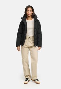 Black puffer jacket with a high collar, worn over a cream sweater and beige wide-leg pants. The outfit is completed with black and cream sneakers.