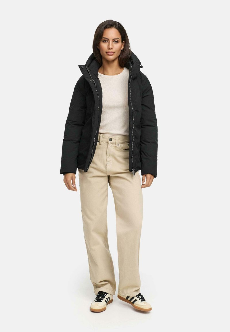 Black puffer jacket with a high collar, worn over a cream sweater and beige wide-leg pants. The outfit is completed with black and cream sneakers.